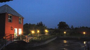 Un bâtiment rouge avec un toit en métal et un petit pont qui y mène. Des lampadaires bordent un chemin, et on aperçoit une étendue d'eau au premier plan.
