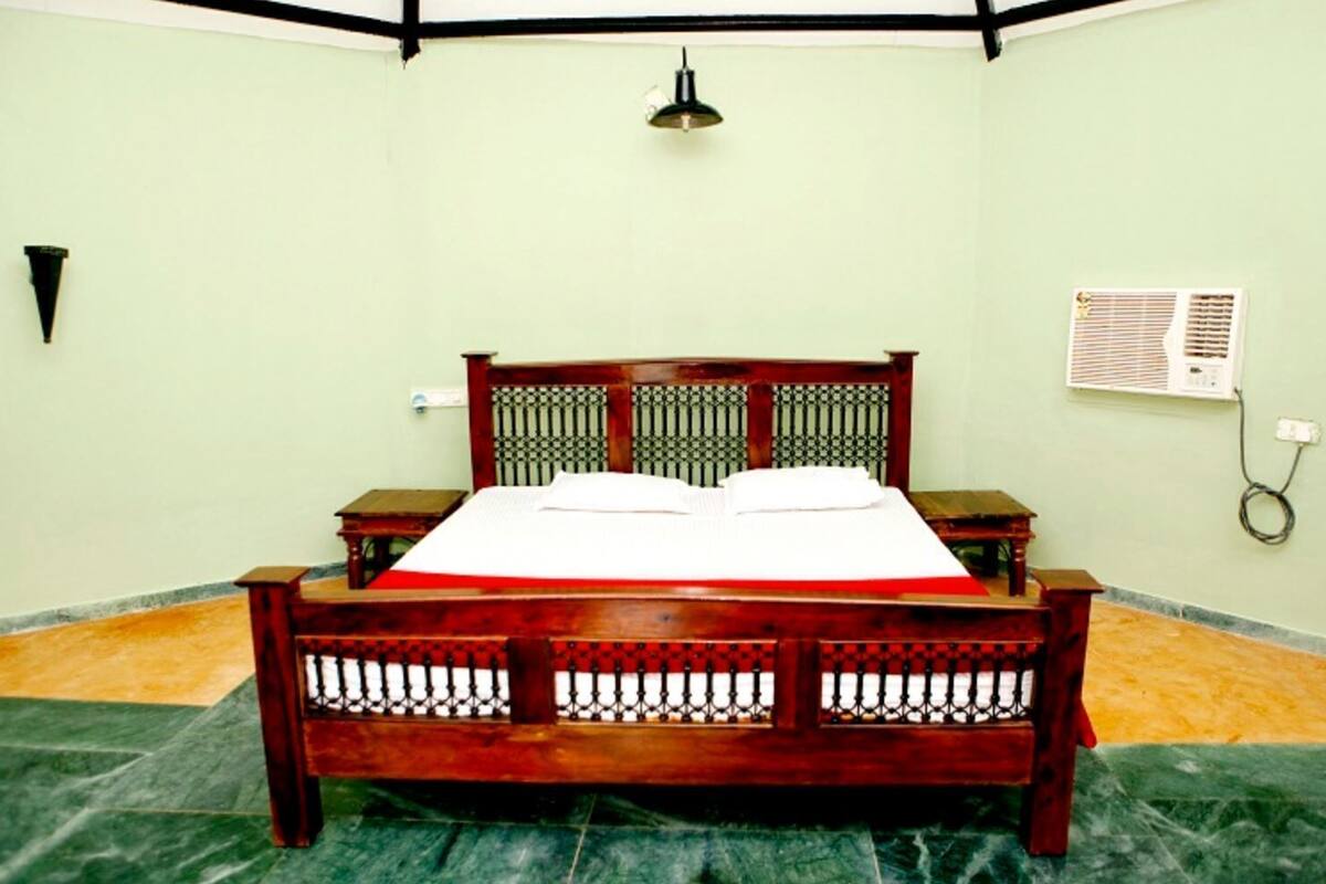 A room with a wooden bed, a small bedside table, a wall-mounted air conditioner, and a light fixture.