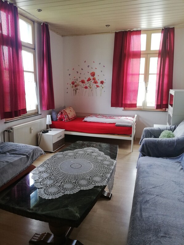 A bedroom with a bed, a sofa, a table with a lace tablecloth, and a radiator.