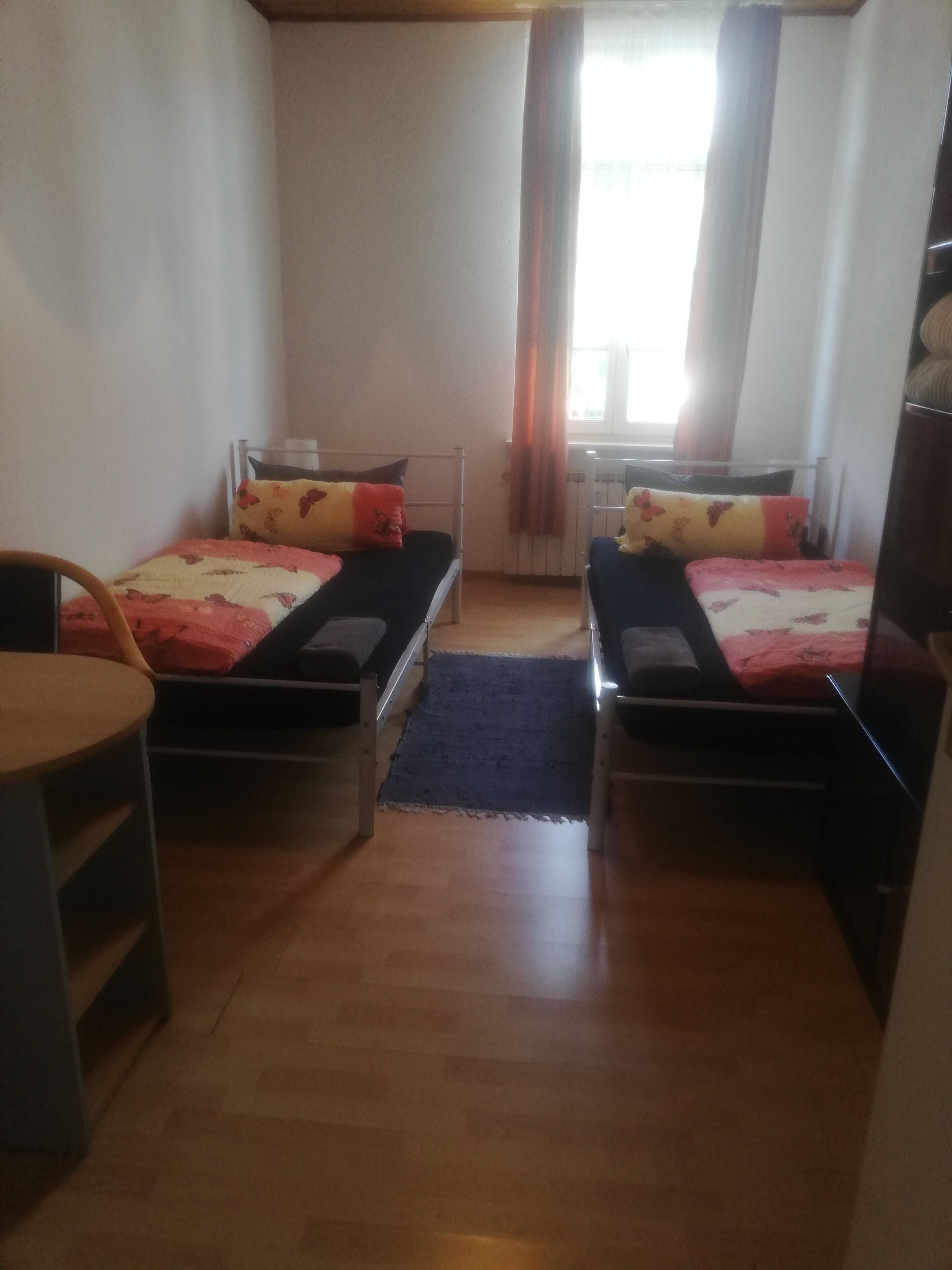A room with two single beds, a small table, and a chair.