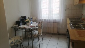 A kitchen with a dining table, chairs, a radiator, and a window with curtains. - Haus Lindheim - Ferienwohnungen (Altenstadt)