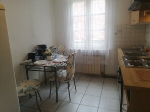 A kitchen with a dining table, chairs, a radiator, and a window with curtains. - Haus Lindheim - Ferienwohnungen (Altenstadt)