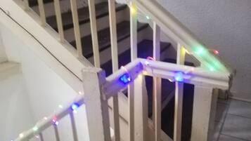 A wooden staircase with a railing, decorated with multicolored string lights.