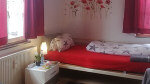 A bedroom with a single bed, a bedside table with a lamp, and a wall decoration of flowers and butterflies. - Haus Lindheim - Ferienwohnungen (Altenstadt)