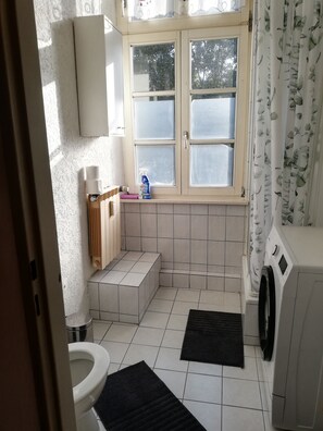 A bathroom with a toilet, a sink, a window, and a washing machine.