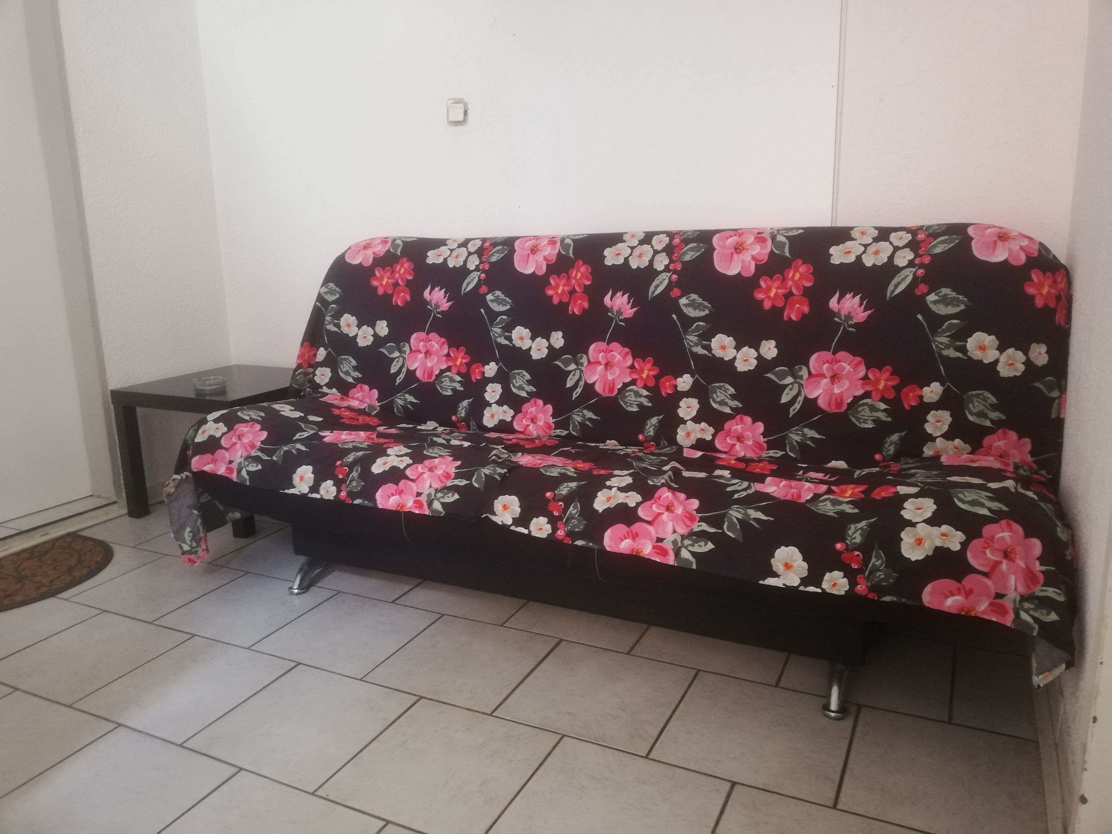 Un canapé de couleur foncée orné d’un motif floral, placé contre un mur blanc.