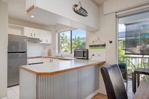 Een moderne keuken met een roestvrijstalen koelkast, witte kasten, een houten aanrechtblad en uitzicht op palmbomen door een groot raam.