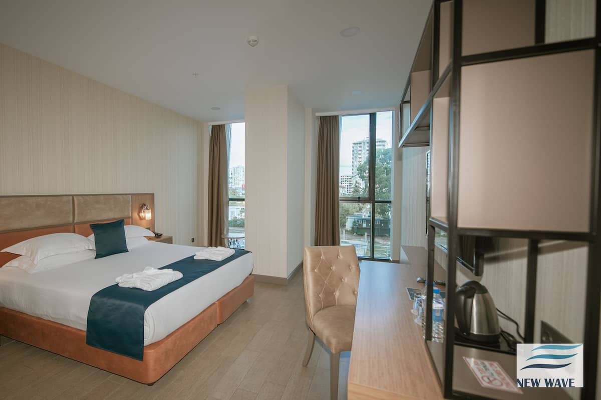 A hotel room with a large bed, bedside tables, a desk, and a view of the city.