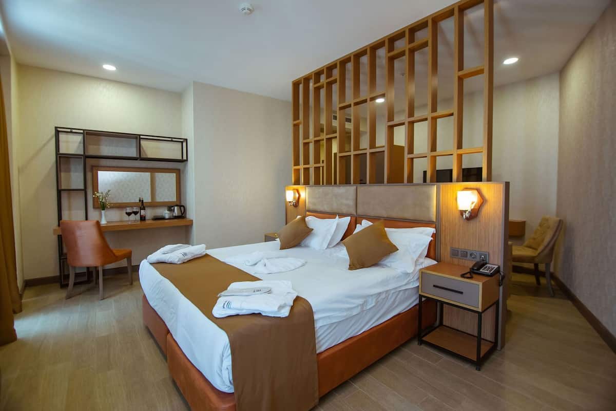 A hotel room with a large bed, a desk with a chair, a bedside table with a phone, and a wall-mounted TV.