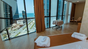 A hotel room with large windows, a bed, a table with a tablecloth, and a chair.