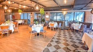 A restaurant with wooden flooring, tables set for dining, hanging plants, and a brick wall.