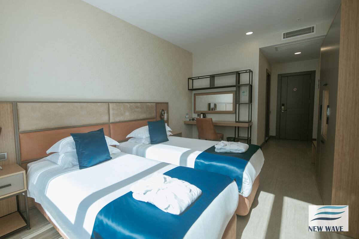 A hotel room with two beds, a desk, a chair, and a bathroom.