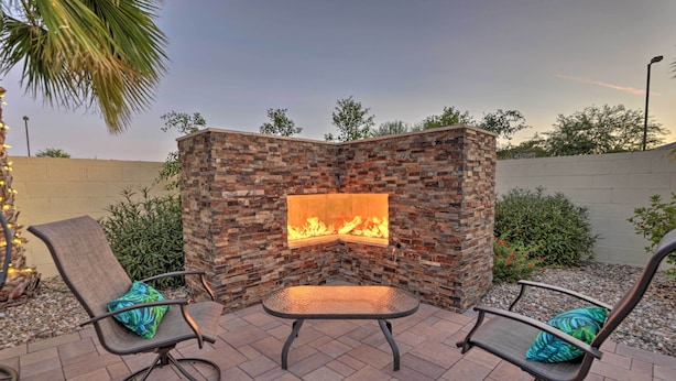 An outdoor seating area with a stone wall and a fire feature. - Modern Azure Home w/ Beautiful Patio, Pool & Spa! (Goodyear)