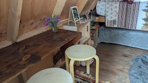 Un intérieur en bois avec un banc en bois, un petit tabouret, un vase de fleurs et un panneau d’affichage noir.