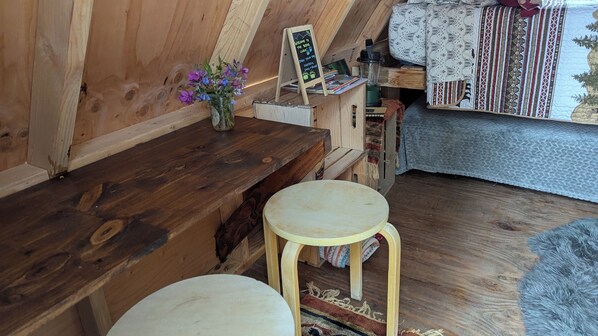 Un intérieur en bois avec un banc en bois, un petit tabouret, un vase de fleurs et un panneau d’affichage noir.