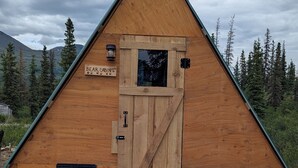 Une cabane en bois avec un toit triangulaire, une porte en bois et une petite fenêtre.