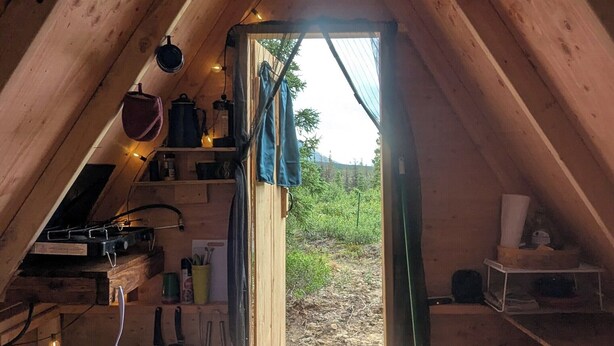 Une pièce mansardée avec un plafond en pente, un petit coin cuisine équipé d’une cuisinière et une porte-fenêtre donnant sur l’extérieur.