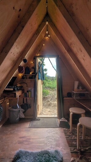 Une pièce mansardée avec un plafond en pente, un petit coin cuisine équipé d’une cuisinière et une porte-fenêtre donnant sur l’extérieur.