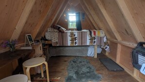 Une chambre mansardée accueillante, avec un lit, une petite table, une chaise et une fenêtre avec des rideaux.