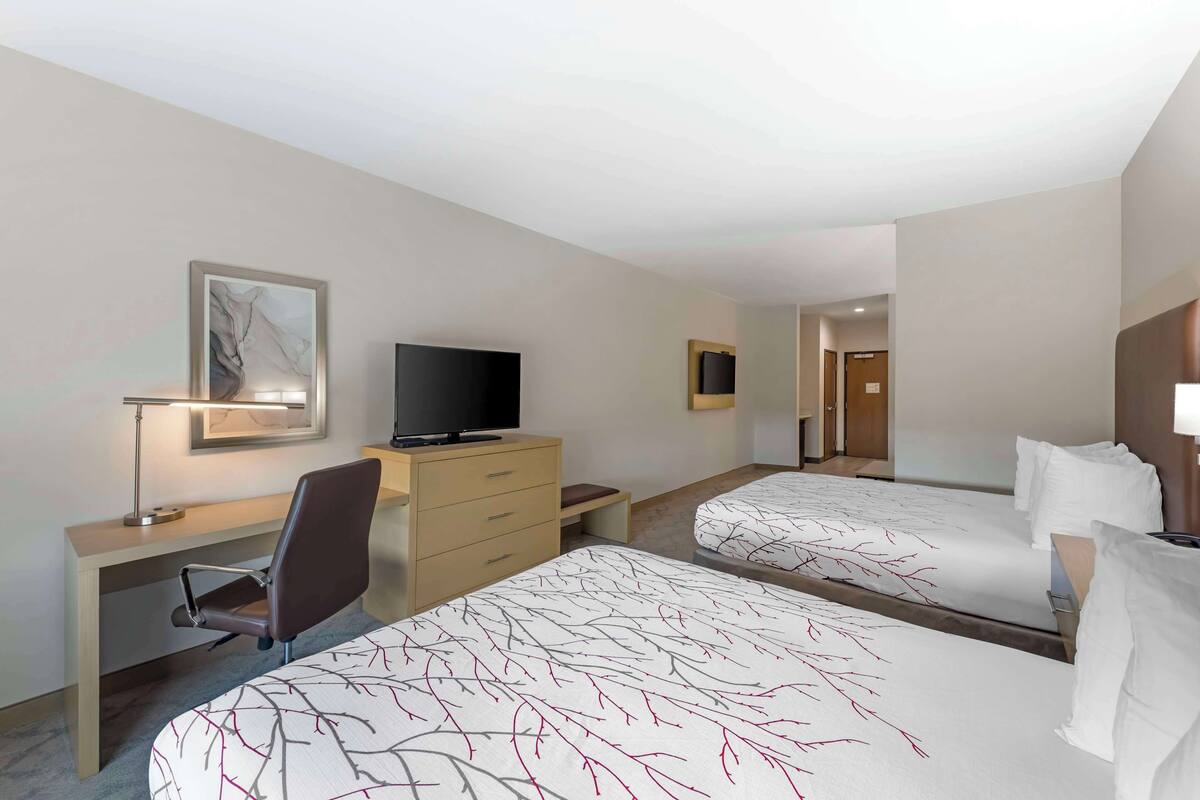 A hotel room with two beds, a desk, a chair, a television, and a painting on the wall.