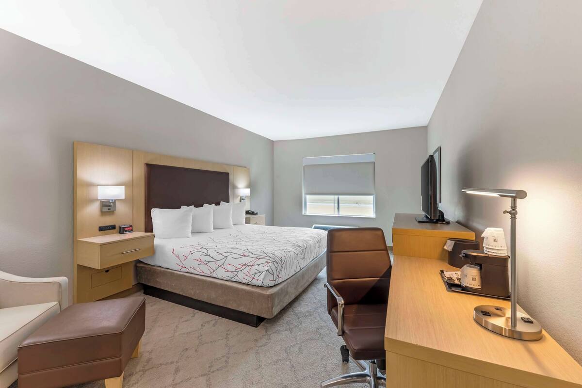 A hotel room with a bed, bedside table, lamp, desk, chair, and a television.