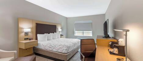A hotel room with a bed, bedside table, lamp, desk, chair, and a television.
