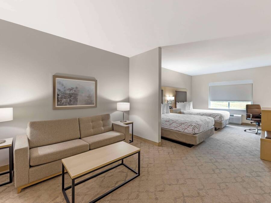 A hotel room with a sofa, a small table, a bed with two pillows, a chair, and a desk.