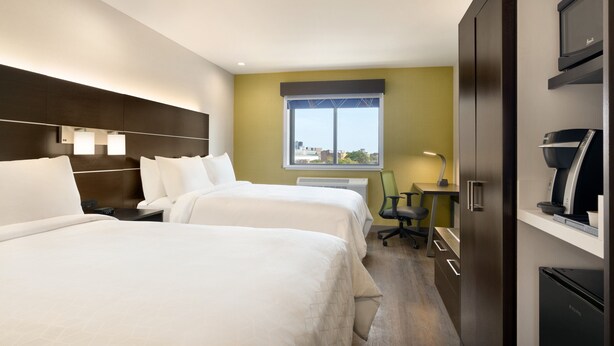 Ein Hotelzimmer mit zwei Betten, einem Schreibtisch, einem Sessel, einem Fernseher und einer Minibar.