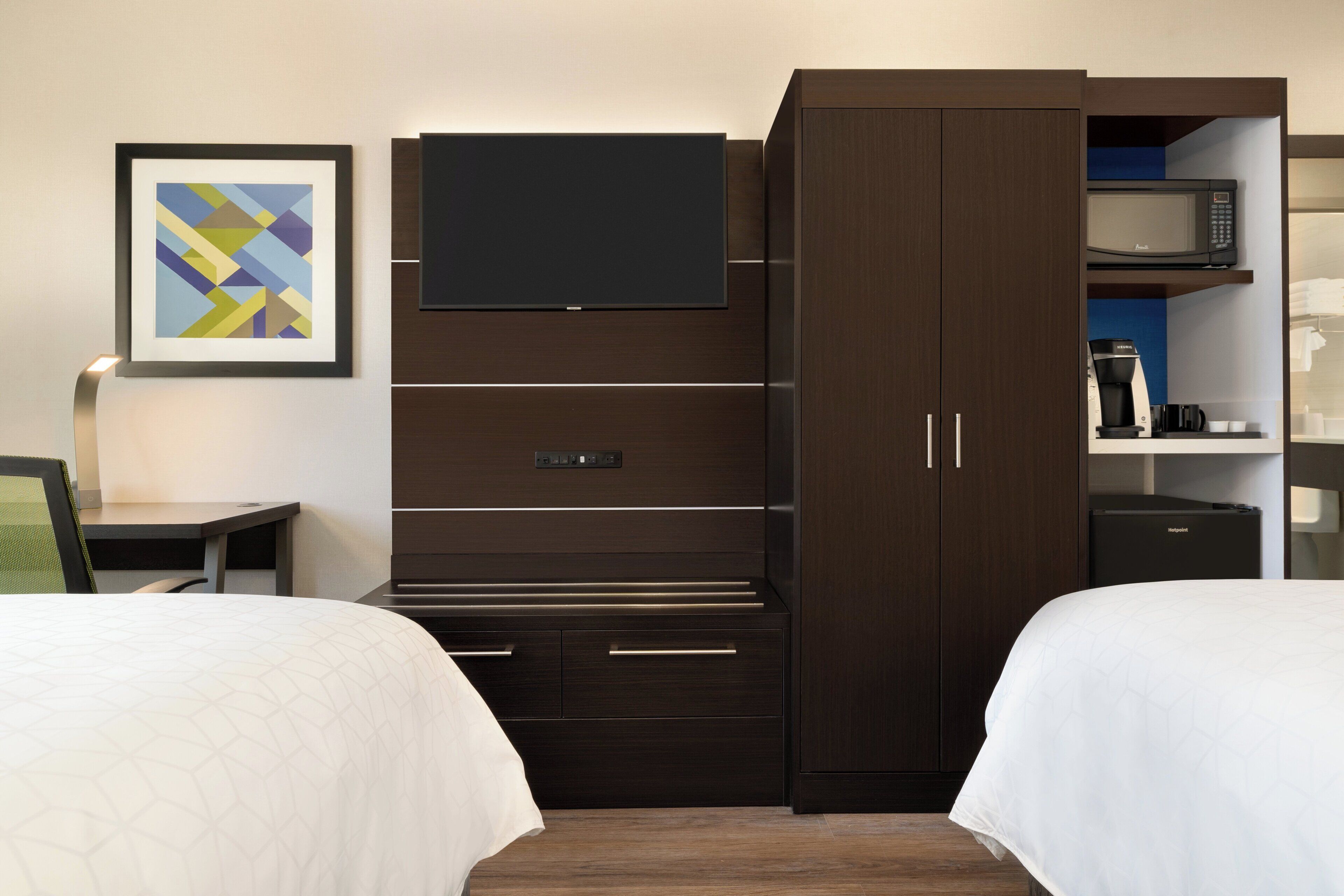 A hotel room with a bed, a desk, a television, a wardrobe, and a coffee machine.