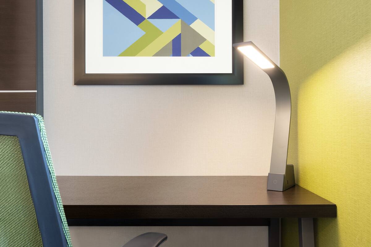 Una taula amb una làmpada moderna, una obra d'art abstracta emmarcada i un monitor informàtic.