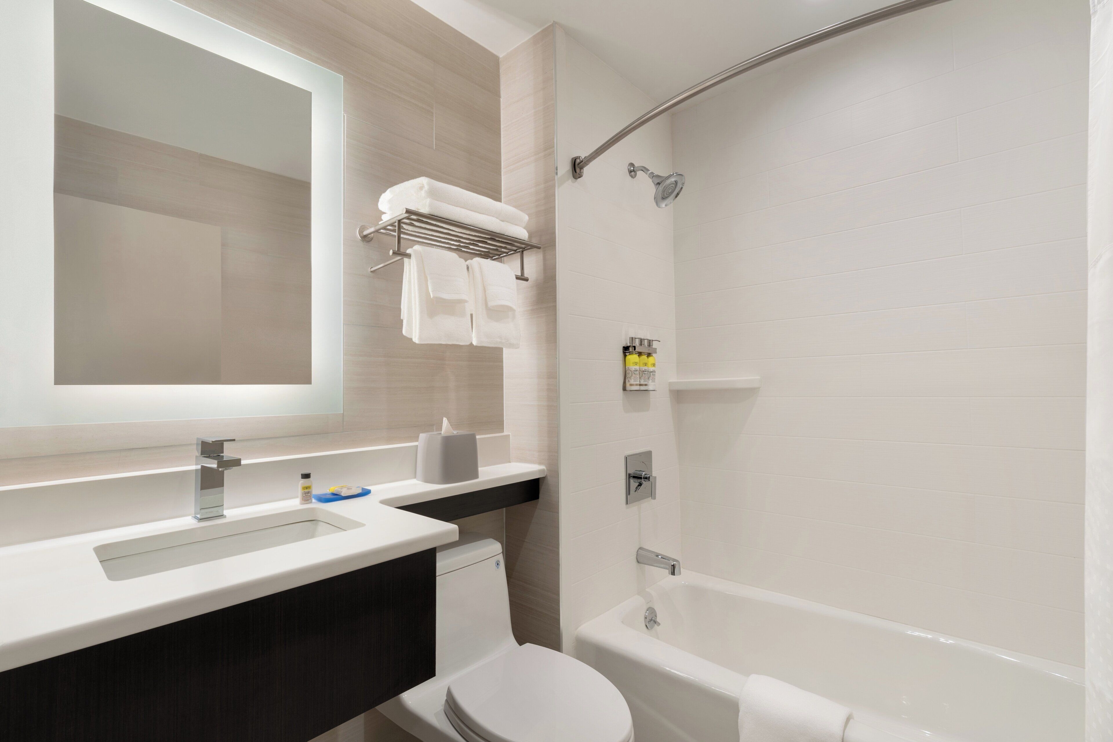 Ein modernes Badezimmer mit Waschbecken, Spiegel, Handtuchhalter, Toilette und Badewanne.