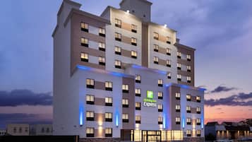 Un hôtel Holiday Inn Express à plusieurs étages, doté d’une façade moderne, de fenêtres illuminées et d’un logo vert bien visible.