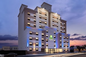 A multi-story Holiday Inn Express hotel with a modern facade, illuminated windows, and a prominent green logo.