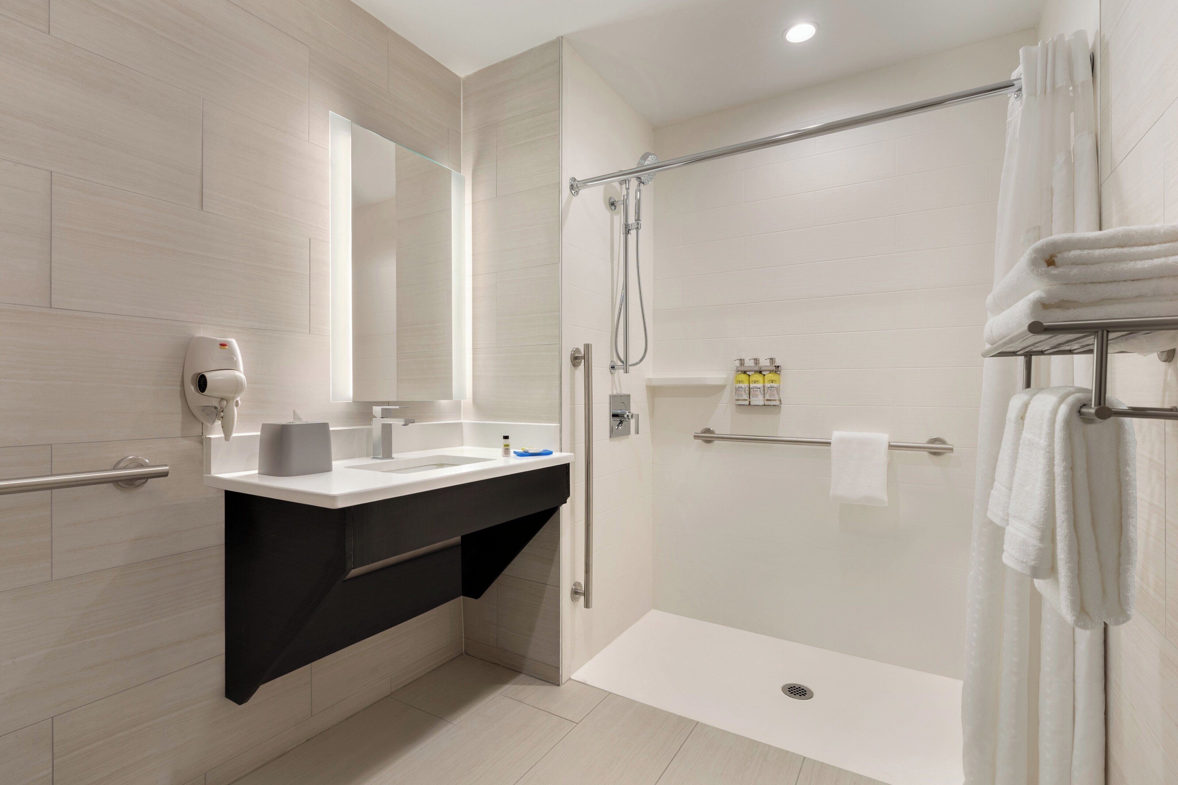 A modern bathroom with a glass-enclosed shower, a vanity with a black countertop, and a towel rack with folded towels.