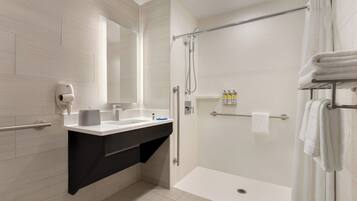 Un baño moderno con cabina de ducha acristalada, un lavamanos con encimera negra y un perchero con toallas dobladas.
