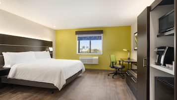 A hotel room with a bed, a desk, a chair, a window with a city view, and an air conditioner.