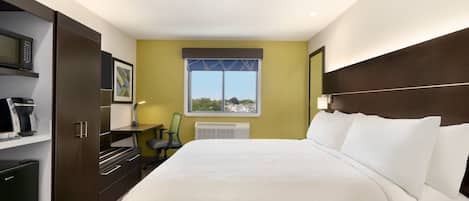 A hotel room with a large bed, a desk with a chair, a microwave, and a small refrigerator.