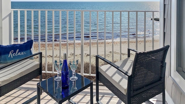 Ein Balkon mit Blick auf das Meer, ausgestattet mit einem Glastisch, zwei Stühlen und einem blauen Kissen mit der Aufschrift 'Relax'.