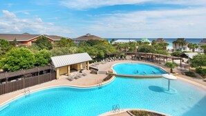 Une grande piscine avec une terrasse en bois et des chaises longues, entourée de maisons et offrant une vue sur l’océan.