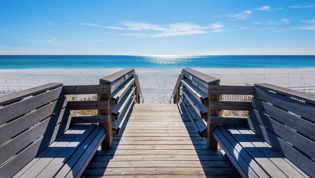Une promenade en bois qui mène à une plage, avec un ciel bleu dégagé.