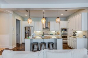 A modern kitchen with white cabinetry, a central island with stools, stainless steel appliances, and pendant lighting.