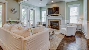 A living room with a fireplace, white furniture, and a television mounted above it. - Spacious 2700 Sq Ft 30A Home - Golf Cart and 6 Bikes, Resort Pool - Life's a Beach in NatureWalk (Santa Rosa Beach)