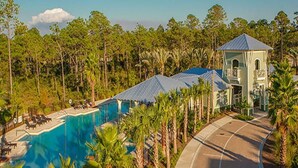 A resort with a swimming pool, palm trees, and a building with a blue roof. - Spacious 2700 Sq Ft 30A Home - Golf Cart and 6 Bikes, Resort Pool - Life's a Beach in NatureWalk (Santa Rosa Beach)
