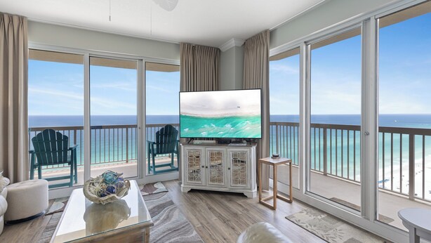 A balcony with a view of the ocean, a television, and a seating area with a coffee table and a sofa. - Sunrise 2011 • Gulf-Front 3BR Retreat • Beach Service (Panama City Beach)