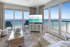 A balcony with a view of the ocean, a television, and a seating area with a coffee table and a sofa.