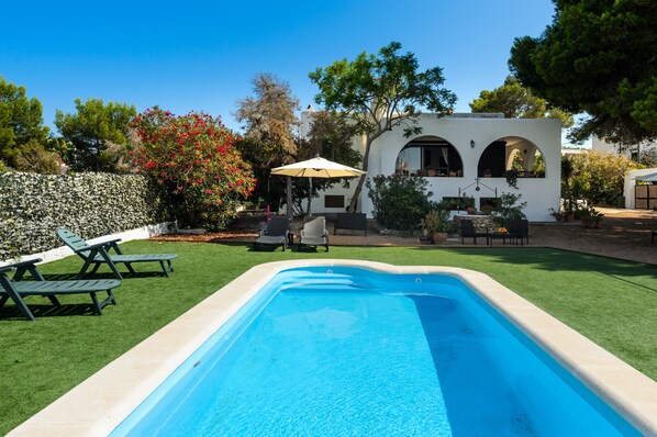 A swimming pool with a white wall, a stone wall, and a tree with red flowers.