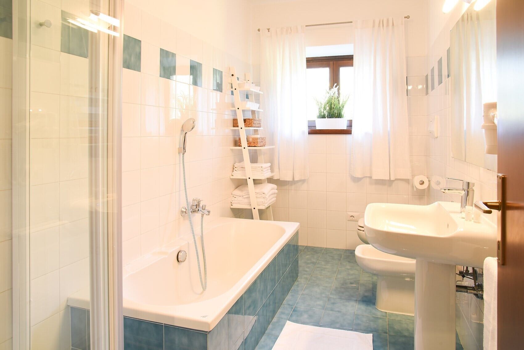 A bathroom with a shower, a bathtub, a sink, and a window with a plant.