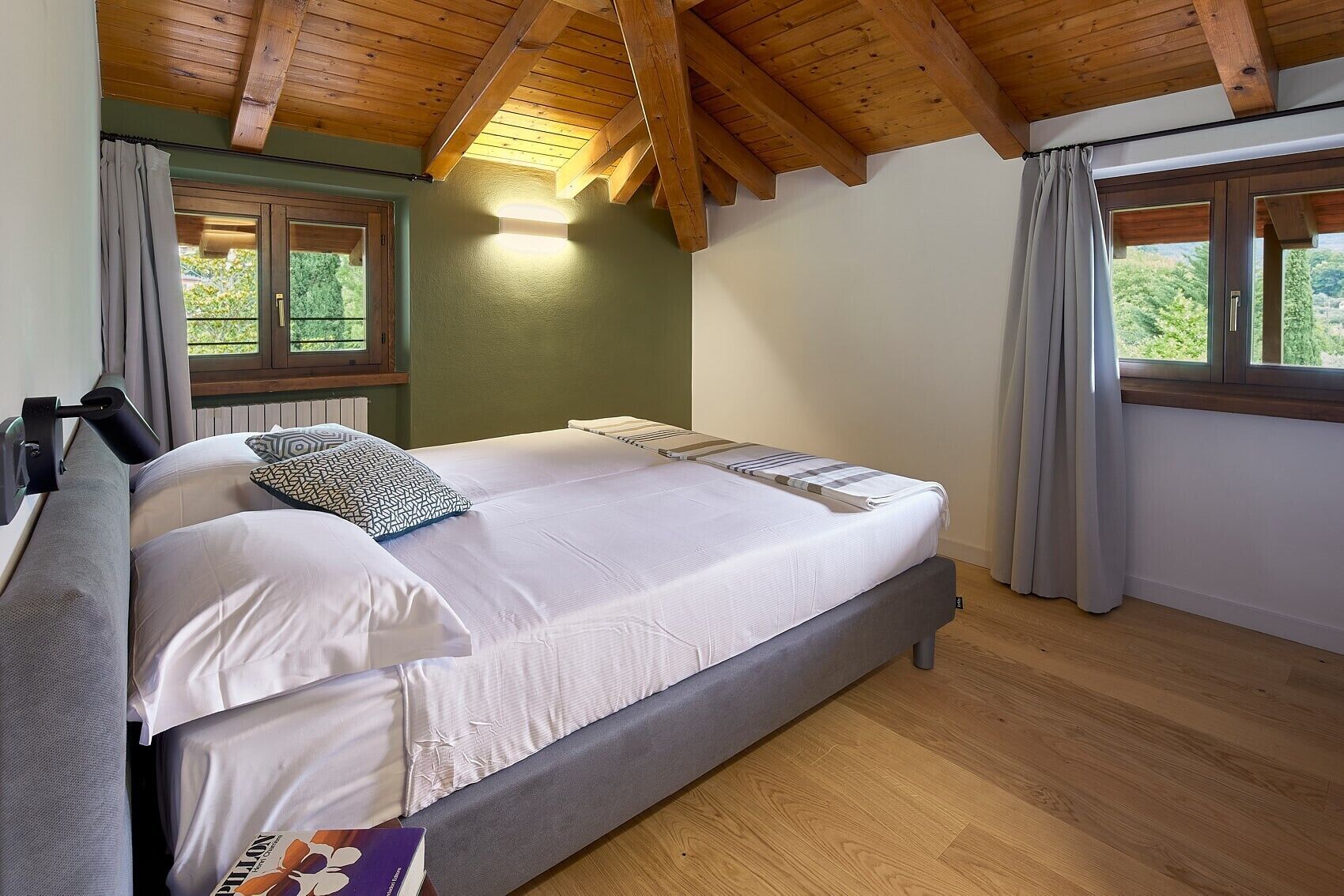 A bedroom with a bed, a bedside table, a lamp, a window, and a view of greenery.
