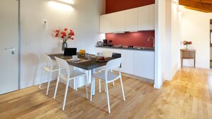 Une cuisine moderne avec des meubles blancs, une table à manger en bois et des chaises blanches, ainsi qu’un mur d’accent rouge.