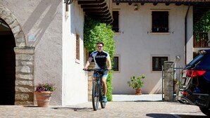 Un cycliste sur un chemin pavé, un bâtiment doté d’une arche en pierre et une voiture garée.